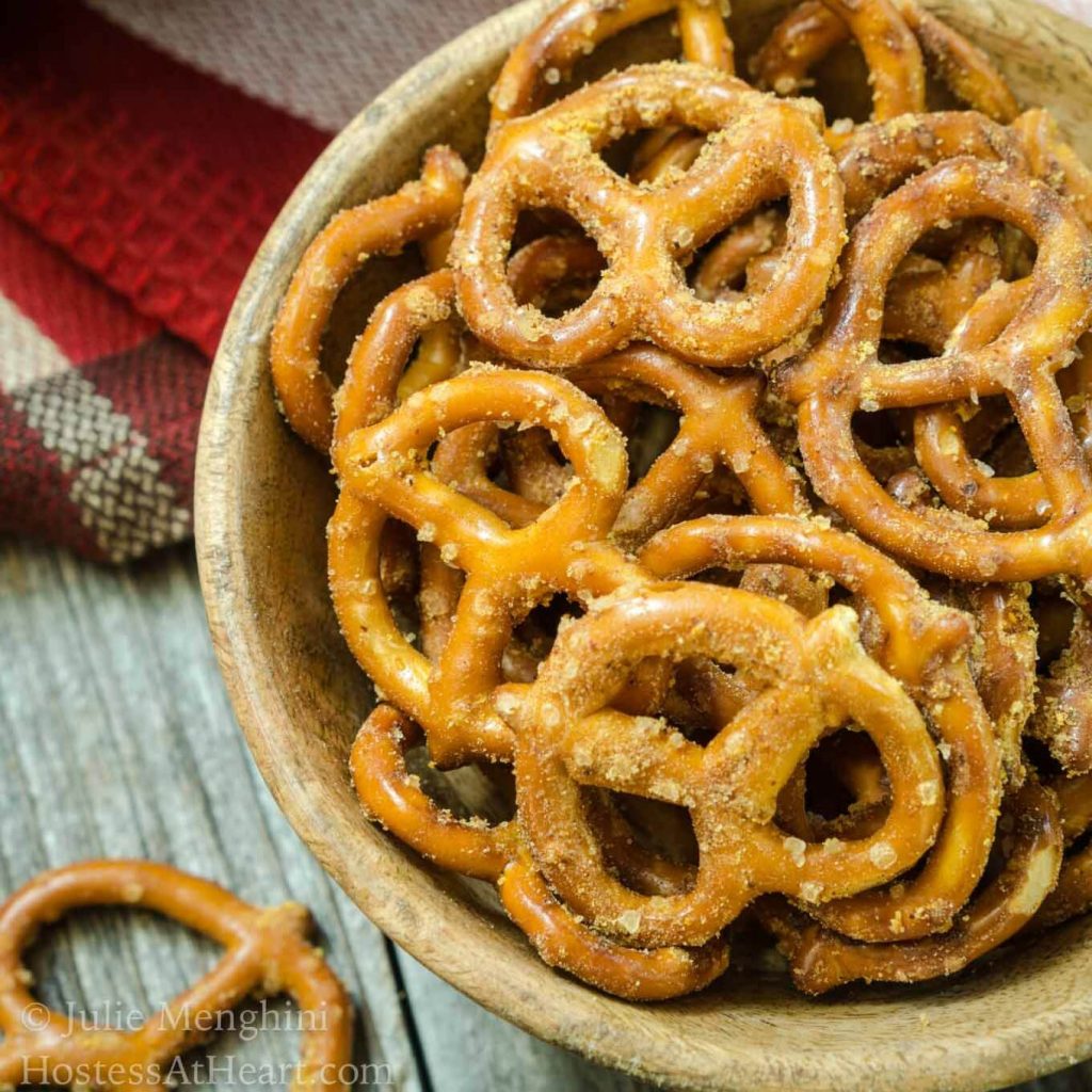 Top-down view of a wooden bowl filled with Spicy Nacho Cheese Pretzels over a red striped napkin. A pretzel sits in the foreground.