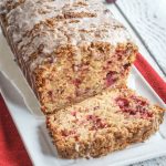 Angled view of 3/4 a loaf of cranberry apple streusel bread on a white plate.