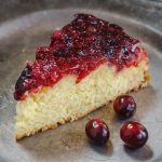 Cut piece of a Cranberry Upside-Down Cake on a metal plate with raw cranberries in the fore front.