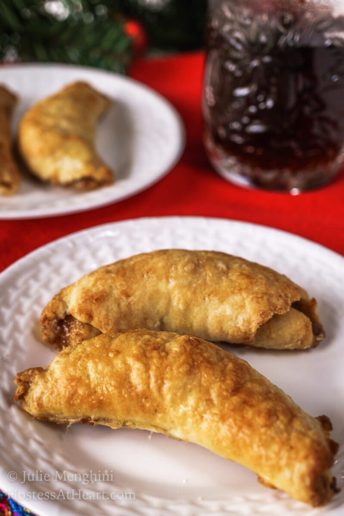 A white plate holding two nut rolls over a red napkin. Another plate of rolls and a cup of coffee sit in the background.