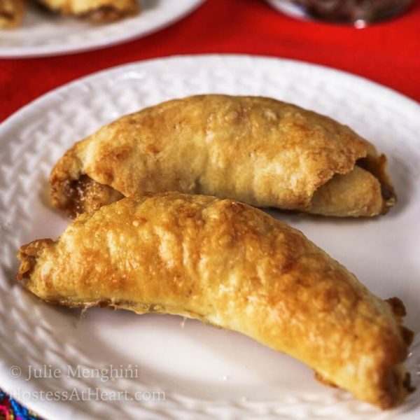 Two crescent nut rolls sitting on a white plate over a red napkin. Another plate of rolls sits in the background.