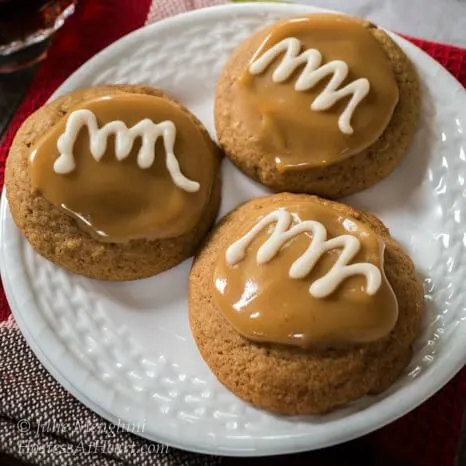 Top-down view of three Spiced Coffee Cookies topped with caramel and a white swirl glaze sitting on a white plate.