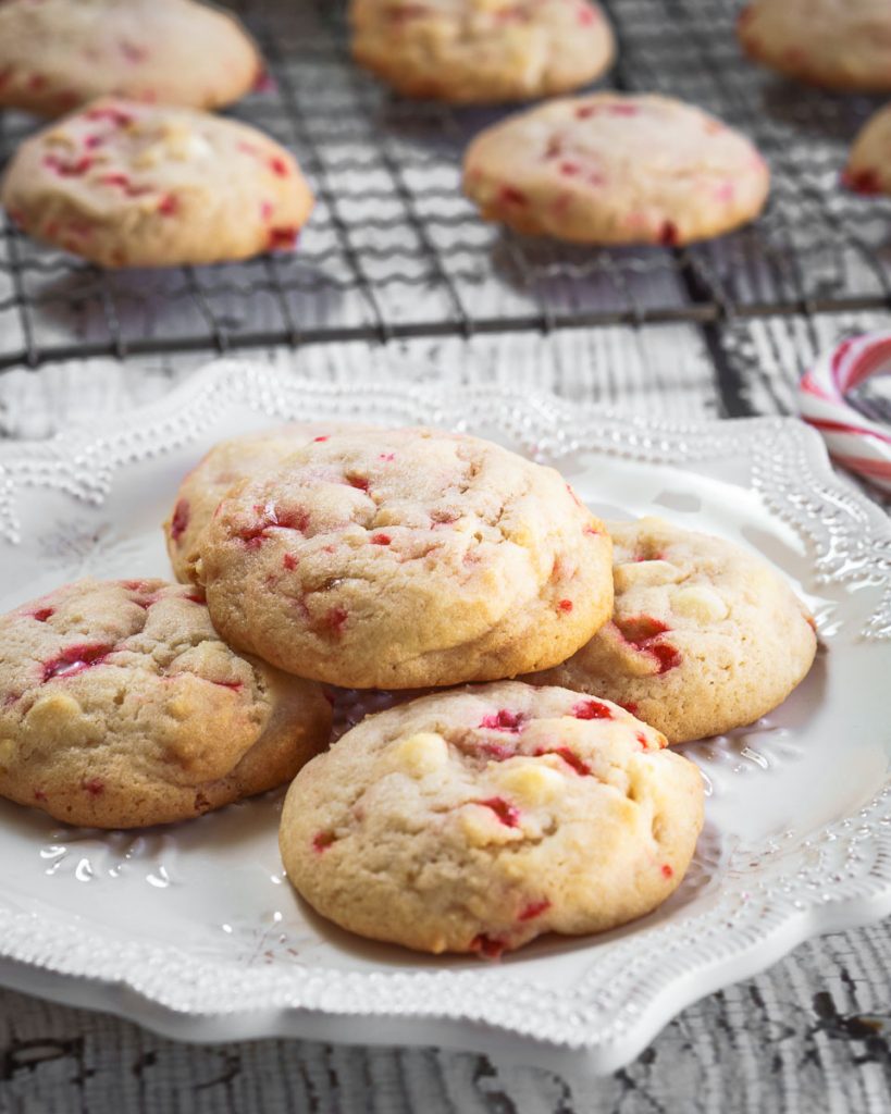 4 cookies stacked on a white snowflake plate with a cooling rack behind it filled with cookies