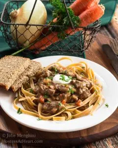 A plate of Beef Stroganoff in front of a basket of vegetables with sliced bread off to the side.