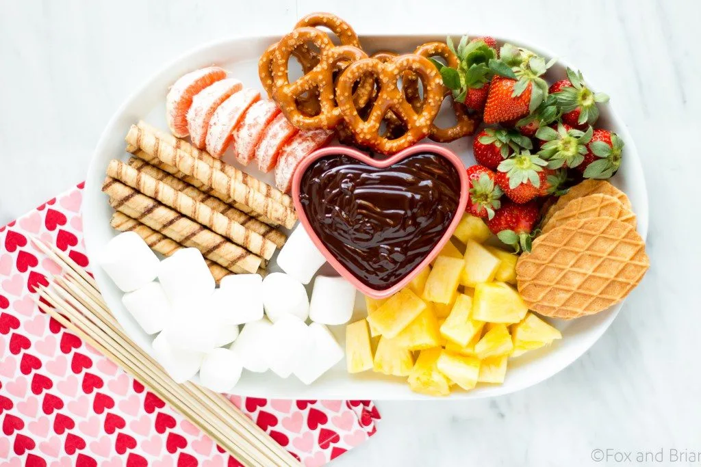 A plate filled with foods used with Chocolate Fondue including pretzels, marshmallows, and strawberries.