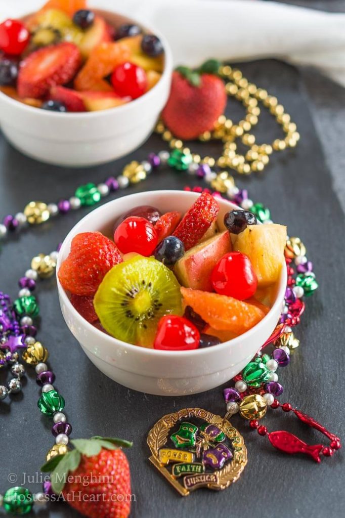 A bowl of Hurricane infused fresh fruit sitting on black slate and surrounded with Mardi Gras beads.