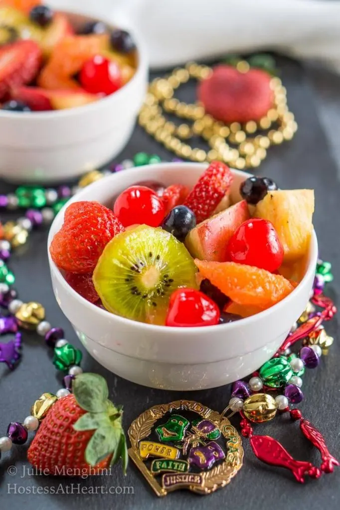 A bowl of Hurricane infused fresh fruit sitting on black slate and surrounded with Mardi Gras beads.