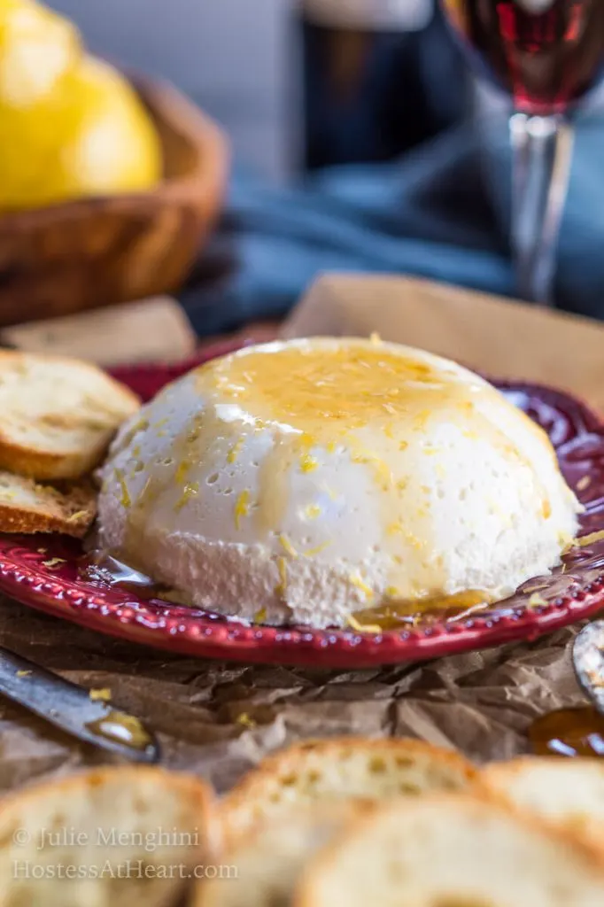 Side view of a mound of homemade ricotta sitting on a red plate and drizzled with honey.