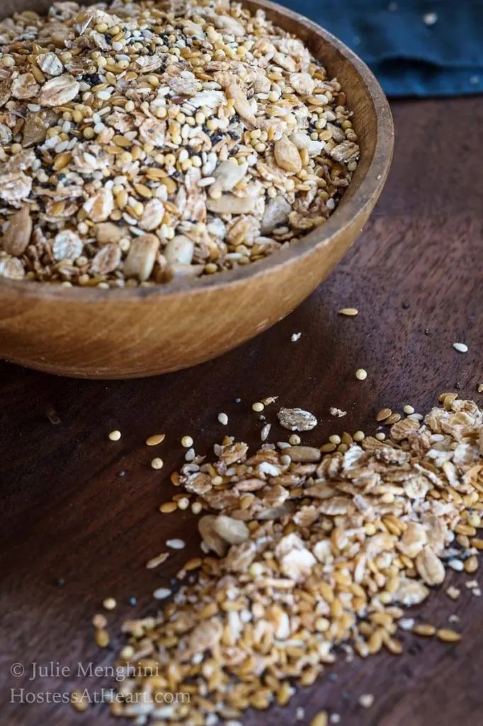 A wooden bowl filled with an Organic Whole Grain Bread Blend with some of the mix scattered on a wooden cutting board.