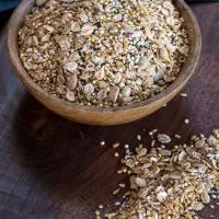 A wooden bowl filled with an Organic Whole Grain Bread Blend with some of the mix scattered on a wooden cutting board.