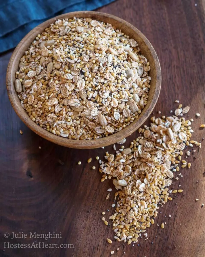 A wooden bowl filled with an Organic Whole Grain Bread Blend with some of the mix scattered on a wooden cutting board.