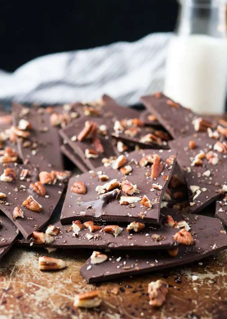 Pieces of homemade pecan chocolate bark are crumbled in front of a glass of milk.