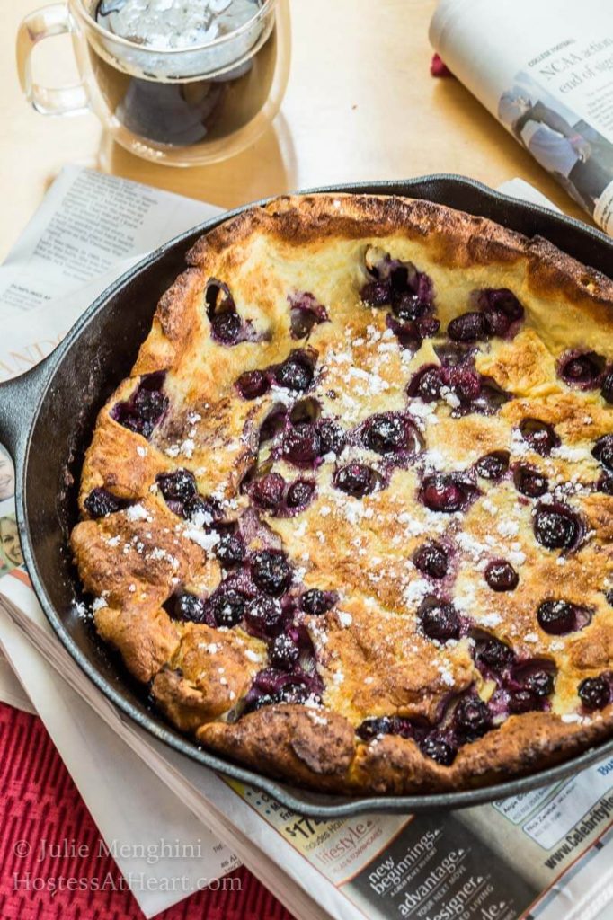 A pan of Blueberry Dutch Baby sitting on the morning newspaper.
