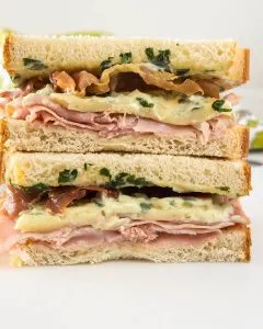 Table view of a sandwich filled with Ham, melted Brie, Prosciutto, and Basil Aioli.