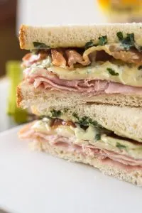 Table view of a sandwich filled with Ham, melted Brie, Prosciutto, and Basil Aioli.