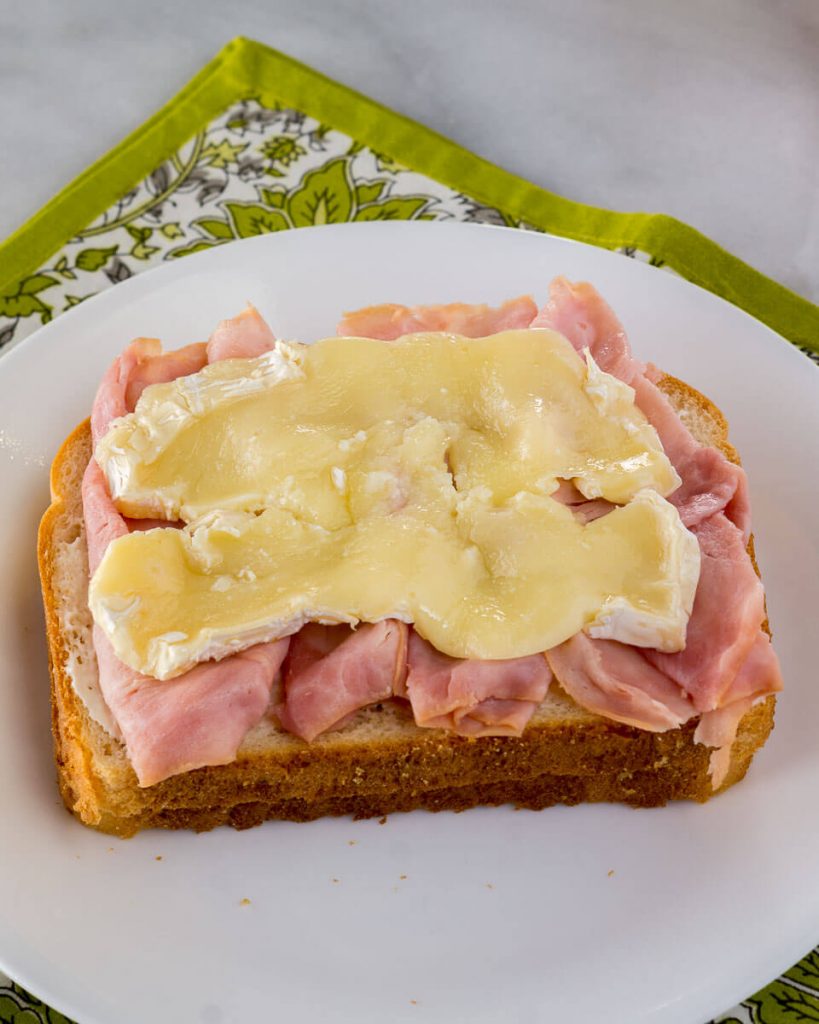A slice of bread topped with shaved ham and Brie.