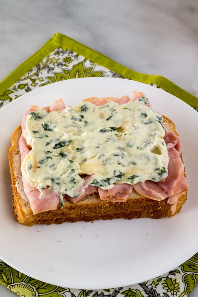 A slice of bread topped with sliced ham, brie, and basil aioli.