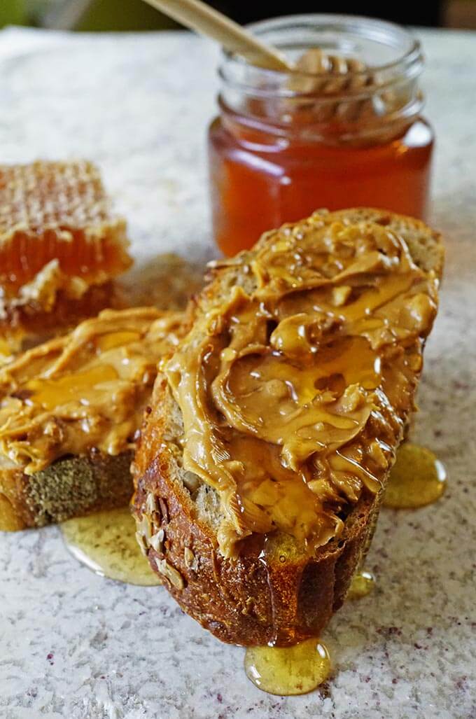 A slice of rustic bread slathered with peanut butter and honey. A jar of honey sits in the background.