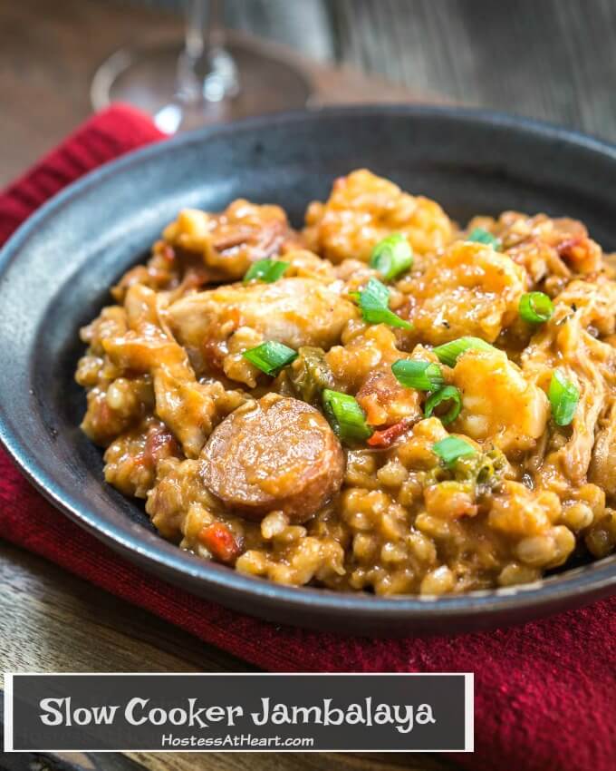 Metal colored bowl over a red bowl filled with Jambalaya made of shrimp and sausage garnished with green onions.