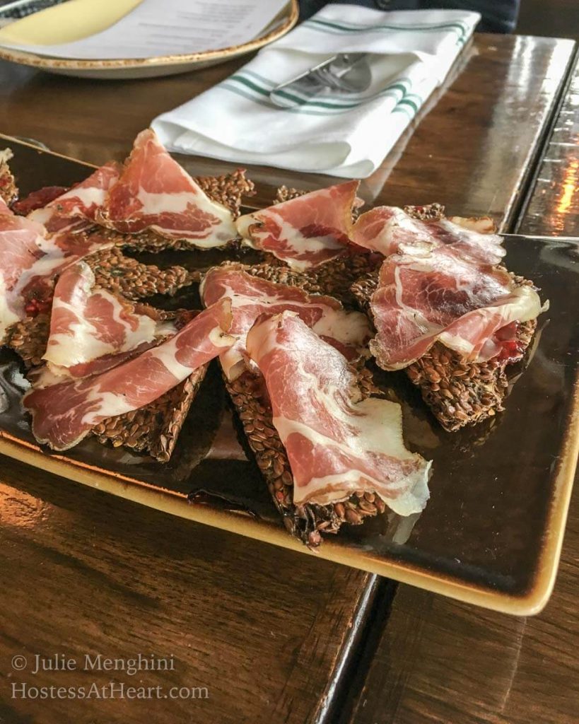 A tray of rustic crackers topped with prosciutto.