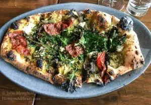 A pizza sitting on a blue plate topped with prosciutto and greens.