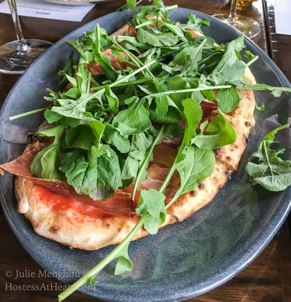 A pizza topped with sauce, prosciutto, and greens on a blue plate.