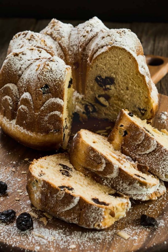 Table view of a Cherry Almond Kugelhopf dusted with powdered sugar. Three slices have been cut and stacked in the front of the loaf.