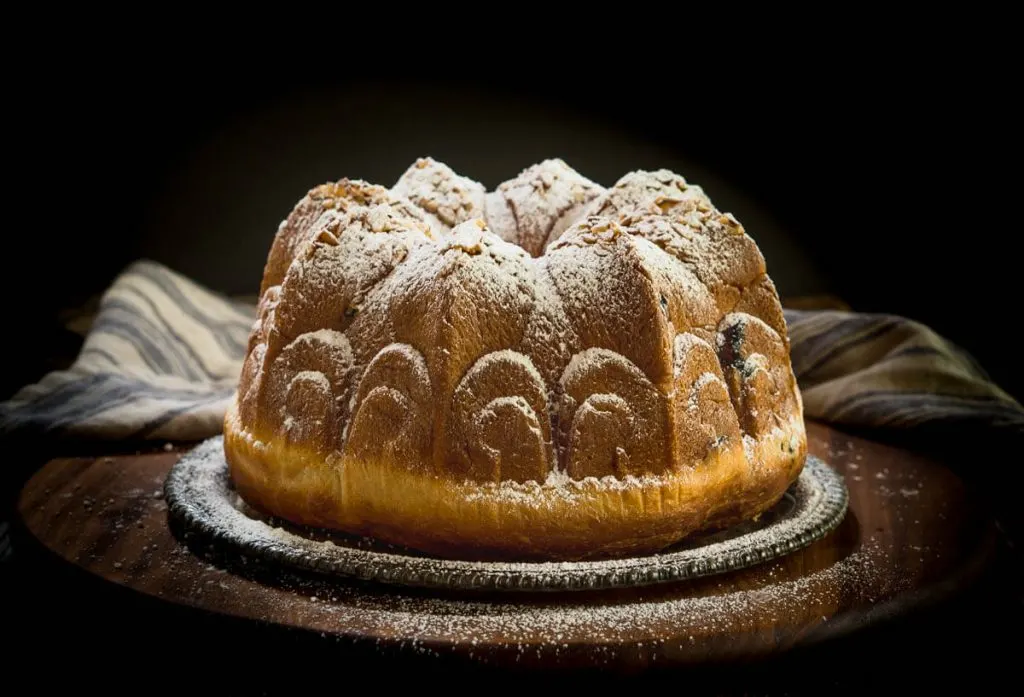 Bundt cake sitting over a silver tray on a wooden cutting board that\'s been dusted with powdered sugar.