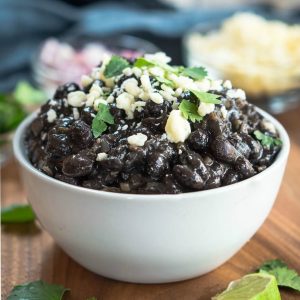 A close up of a bowl filled with black beans that have been garnished with Cotija cheese and cilantro.