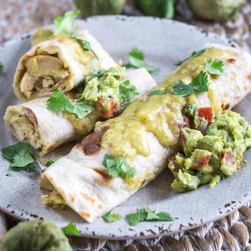 To chicken enchiladas sauced with Green Mole on a gray plate and garnished with guacamole and cilantro.