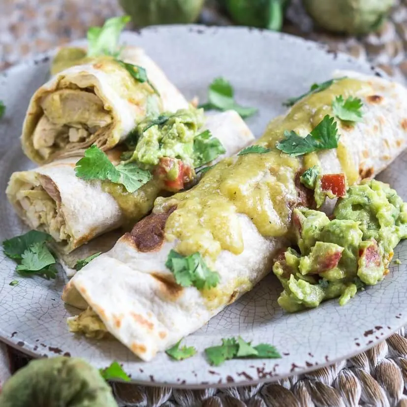 To chicken enchiladas sauced with Green Mole on a gray plate and garnished with guacamole and cilantro.