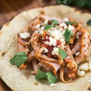 A Taco shell filled with Pork Al pastor and garnished with Cotija cheese and cilantro.