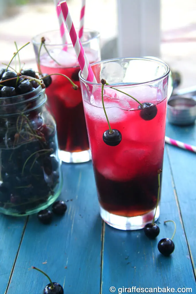 A side view of a cocktail made from cherries. A jar of cherries sit to the side.