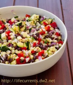 A bowl of salad made up of corn, black beans, red peppers, and red onions.