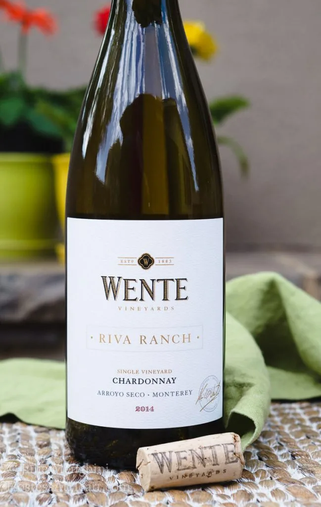 A bottle of Wente wine sitting on a green napkin in front of a pot of flowers.