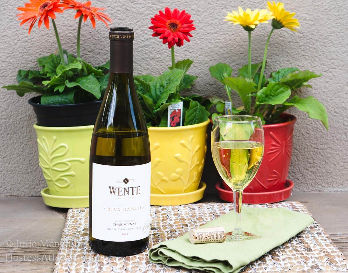 A bottle of wine and a vase of flowers on a table next to a glass of wine.