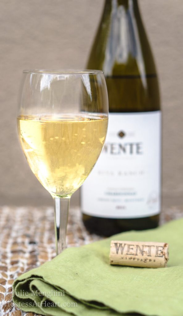 A close up of a glass of wine, with a bottle of Wente Chardonnay.