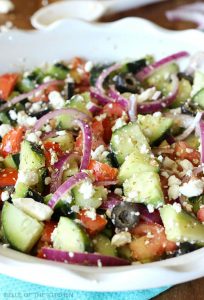 A close up of a plate salad made of tomatoes, black olives, red onion, cucumbers, and feta cheese.