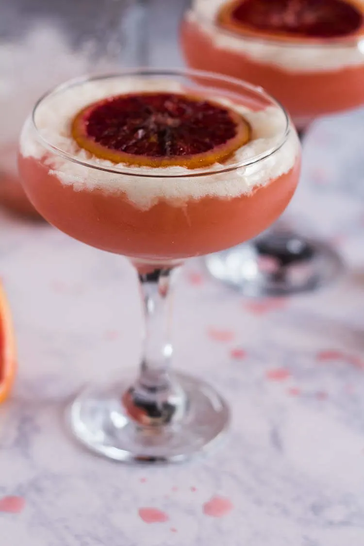 A coup glass filled with a Piso cocktail and garnished with a slice of blood orange.