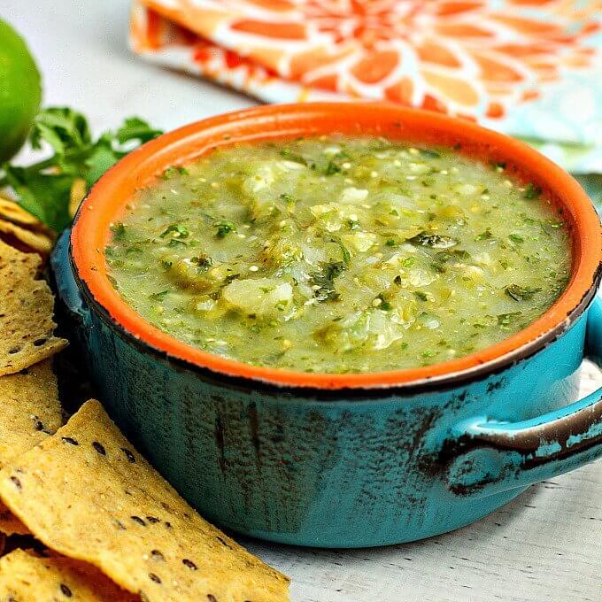 Side view of a turquoise bowl filled with salsa verde. Tortilla chips sit off to the side.