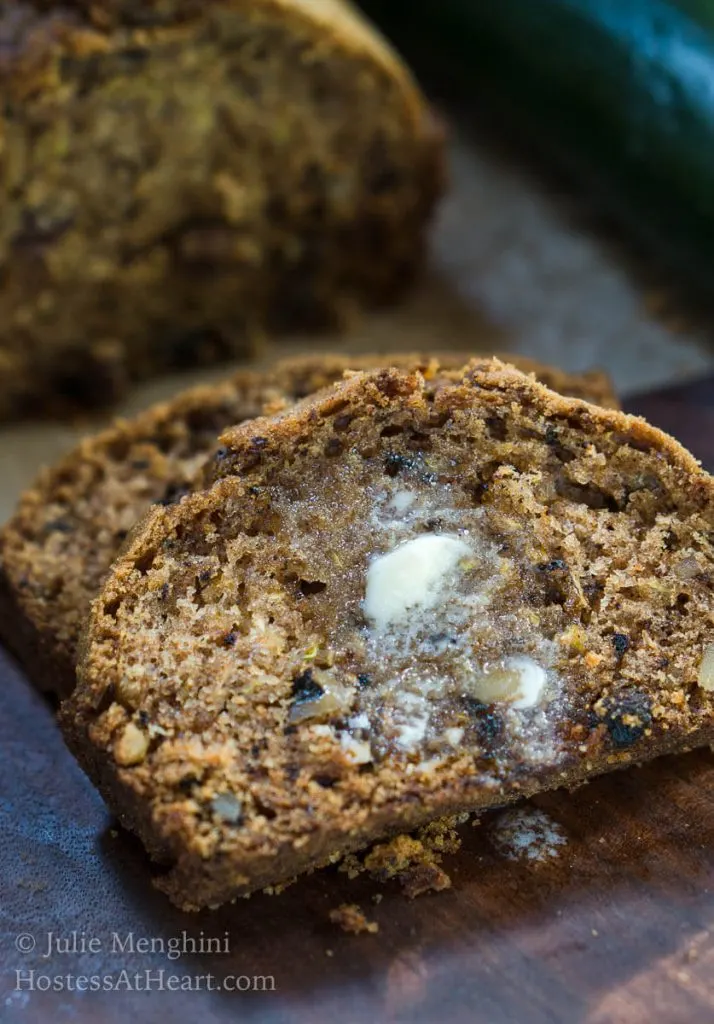 Slices of zucchini bread with melted butter running off the front over a wooden cutting board.