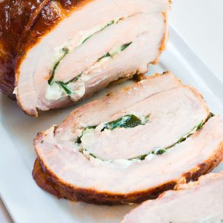 Top-angle view of a pork tenderloin that's been stuffed with goat cheese and spinach, tied and grilled over a white platter.