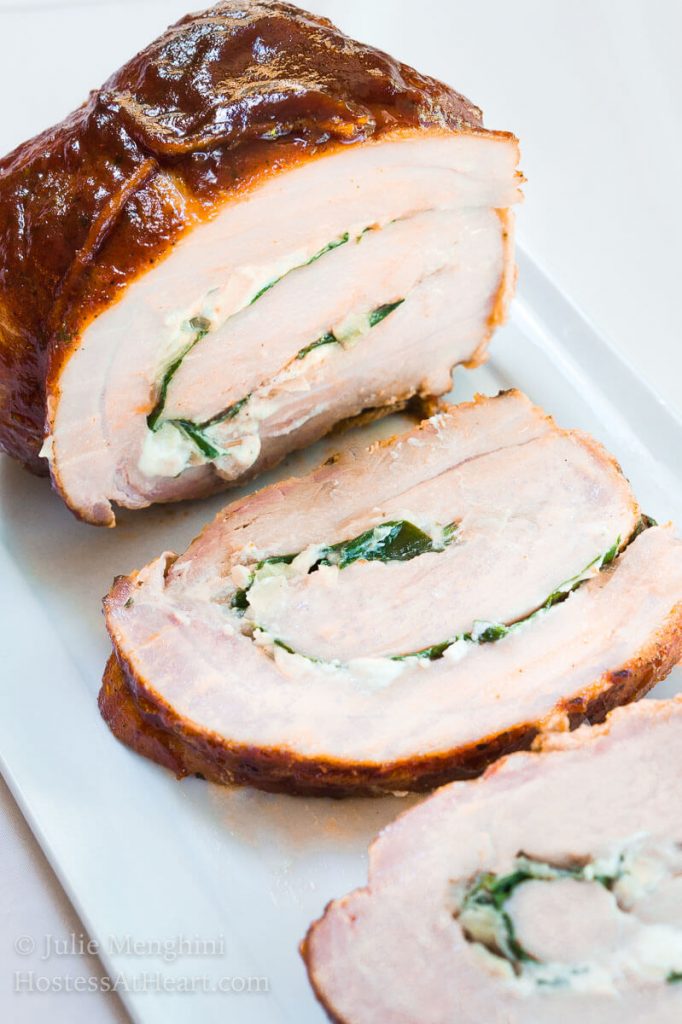 Top-angle view of a pork tenderloin that\'s been stuffed with goat cheese and spinach, tied and grilled over a white platter.