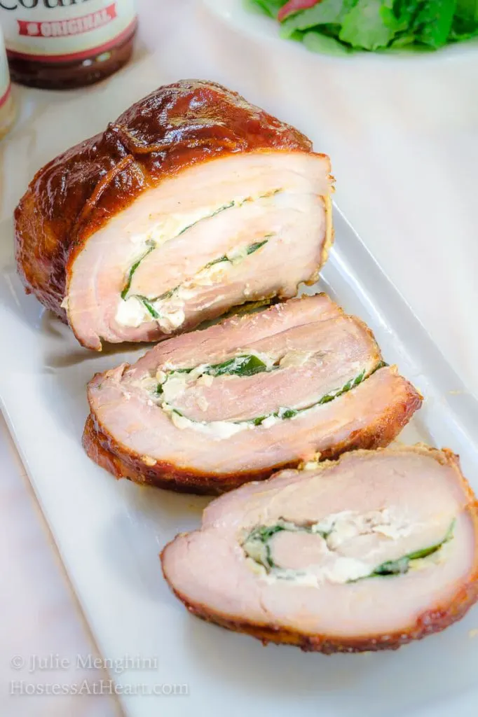 Grilled Pork Tenderloin that\'s stuffed with goat cheese and spinach then tied, grilled, and sliced on a white plate.