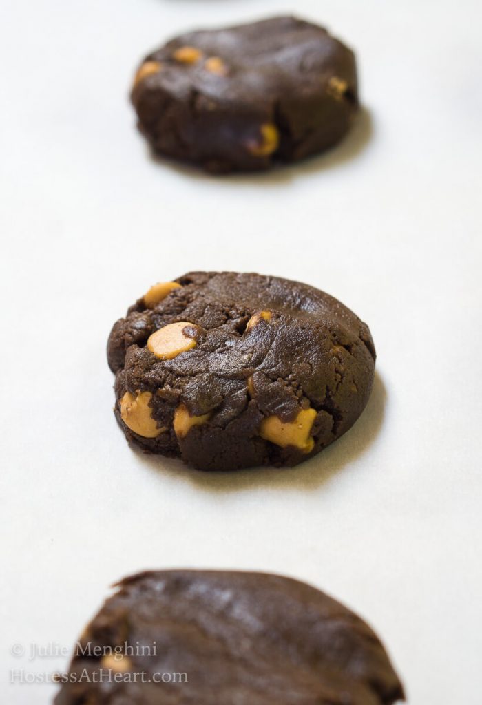 Raw cookie dough of a chocolate cookie dotted with peanut butter chips sitting on white parchment paper.