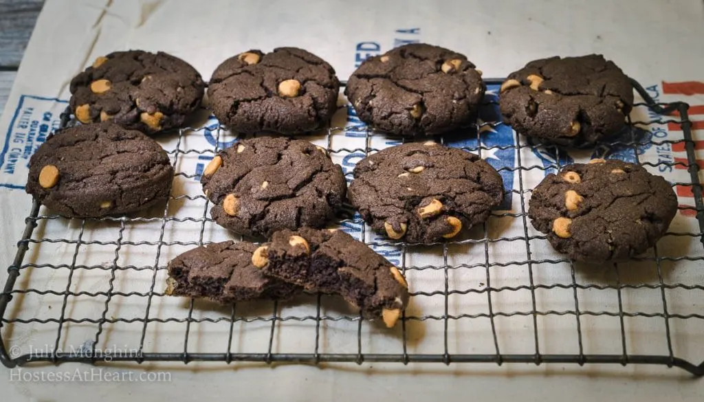 Chocolate cookies dotted with peanut butter chips sit on a cooling rack over a flour sack.