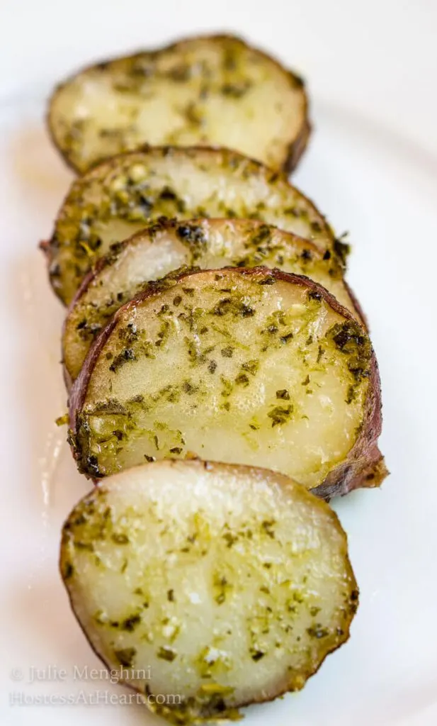 Sliced Hasselback potato with basil garlic sauce sitting on a white plate.