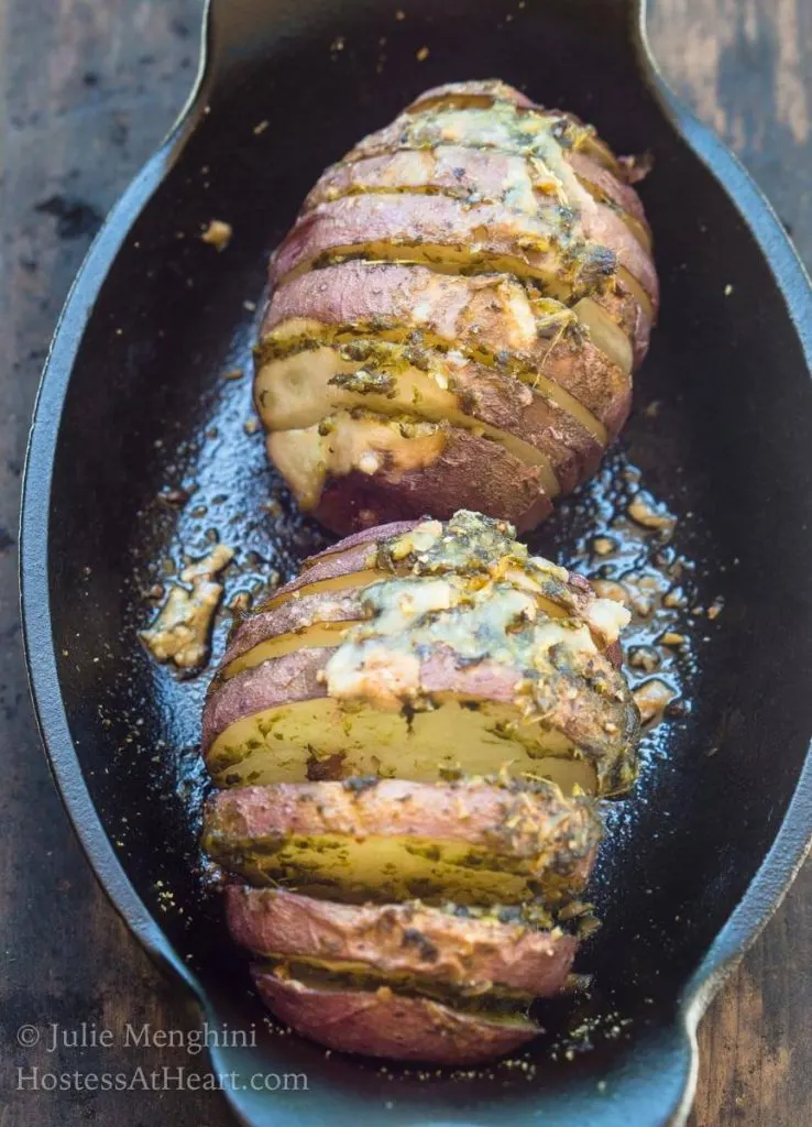 A Hasselback red potato loaded with garlic basil sauce sitting in a cast-iron casserole dish.