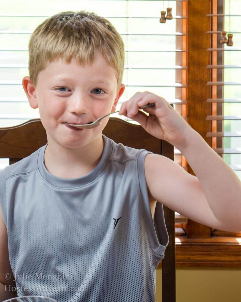 A young boy sitting in front of a window eating ice cream.