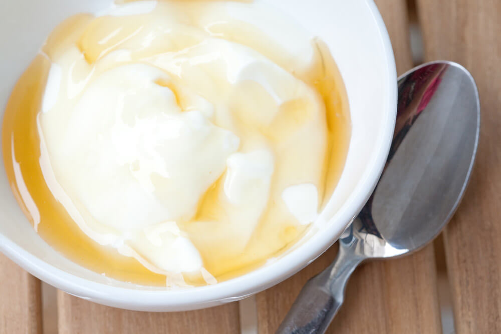 A white bowl filled with yogurt that\'s been drizzled with honey. A spoon sits next to it.